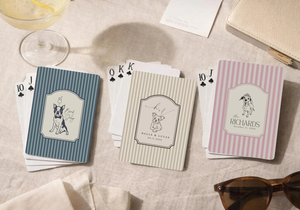 Playing cards with dog illustrations and text on a textured surface with a glass of wine and sunglasses. Wedding Party Favors