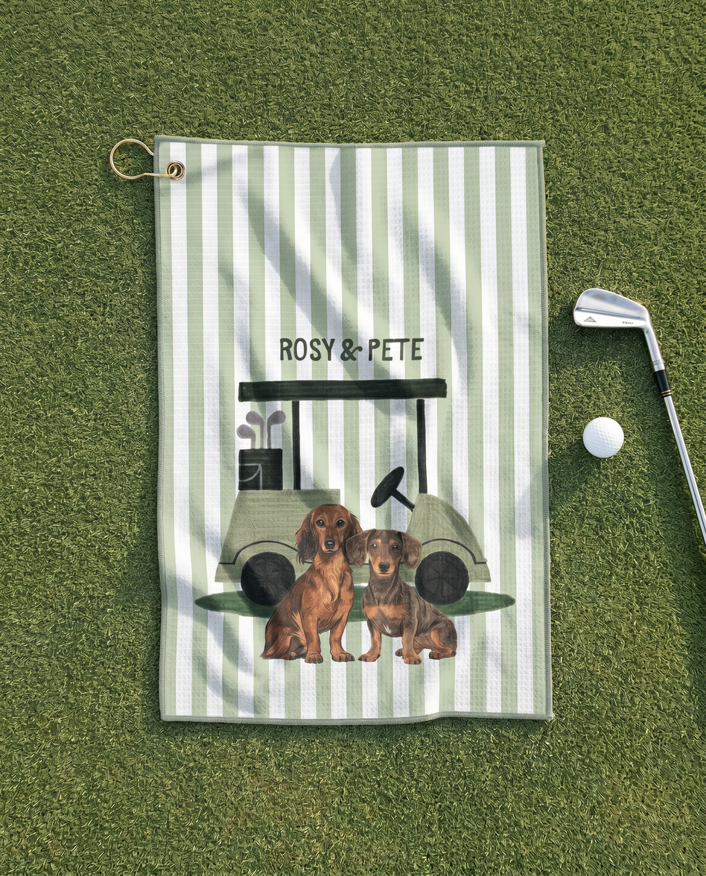Golf towel with dachshunds and golf cart design on a green surface