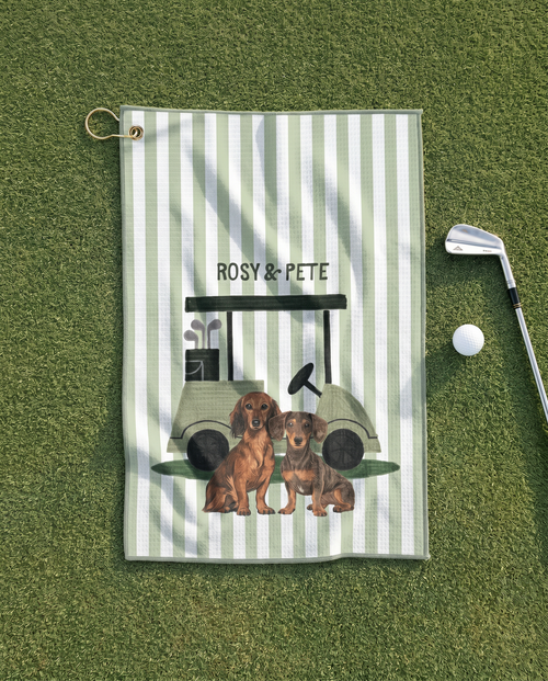 Golf towel with dachshunds and golf cart design on a green surface