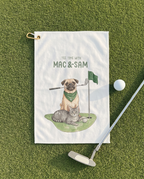 Golf towel with illustration of a pug and cat playing golf, placed on grass with a golf club and ball.