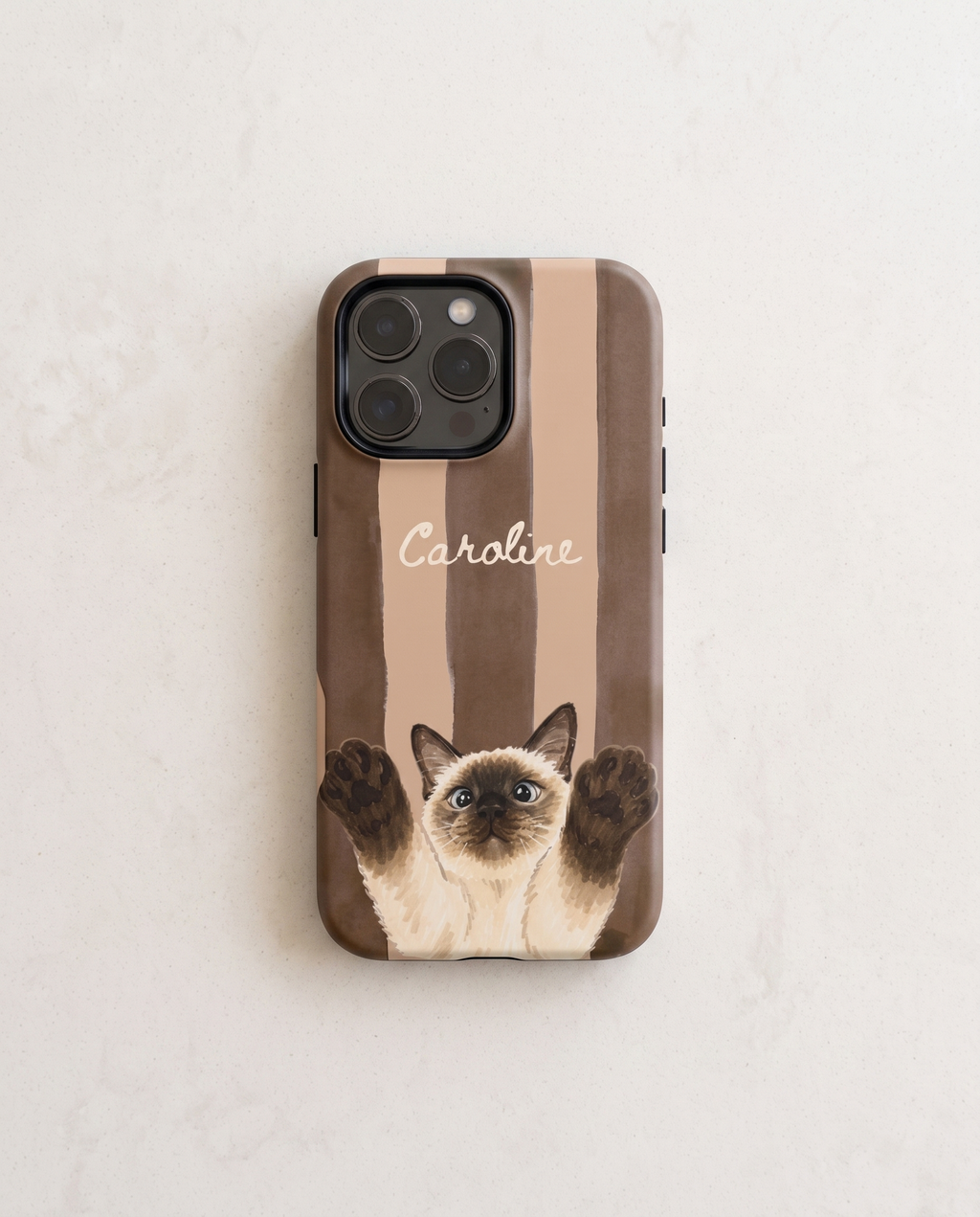 A personalized phone case featuring a brown and beige striped background, a Siamese cat illustration with raised paws, and the name 'Caroline' in white script. The case is shown on a light-colored, textured surface.