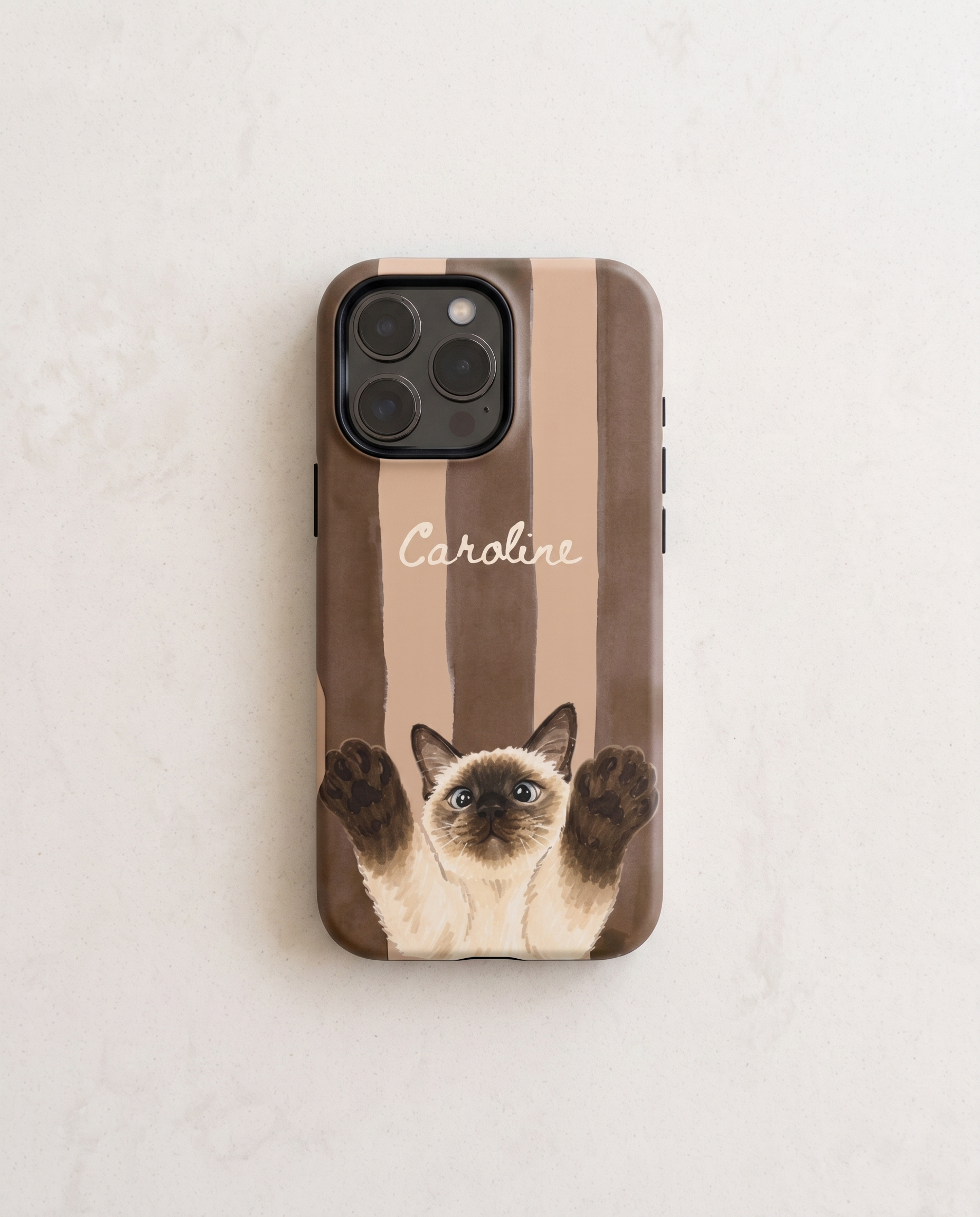 A personalized phone case featuring a brown and beige striped background, a Siamese cat illustration with raised paws, and the name 'Caroline' in white script. The case is shown on a light-colored, textured surface.