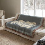 Gray blanket with a bull dog design draped over a beige sofa in a living room.