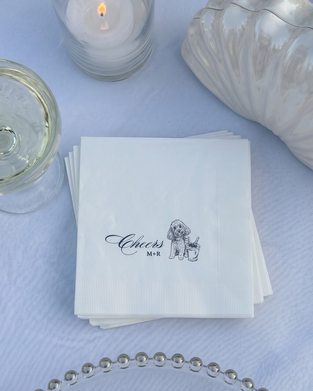 Stack of white napkins with 'Cheers' and a dog illustration on a light blue tablecloth.