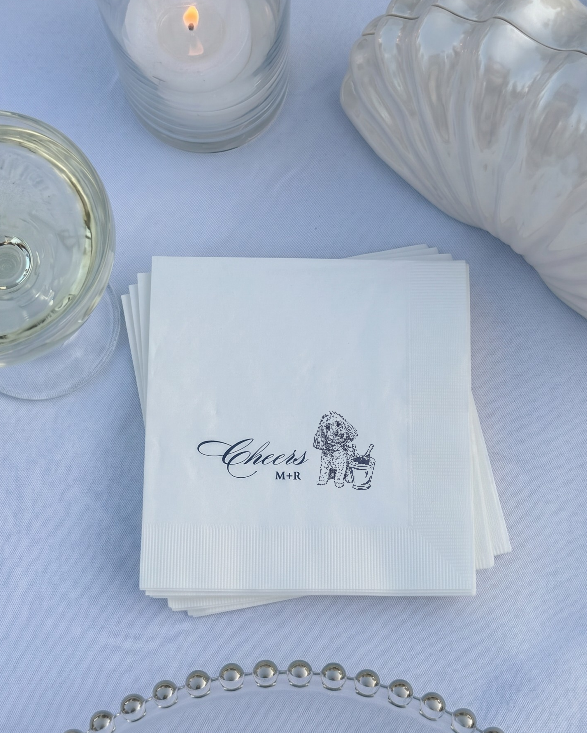 Stack of white napkins with 'Cheers' and a dog illustration on a light blue tablecloth.