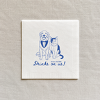 A square white paper napkin with blue line art of a golden retriever and a cat wearing a bow tie, with the text 'Drinks on us!' and a date printed below, displayed on a textured beige linen background.