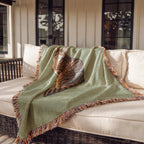 Green blanket with cat and fringe draped over a wicker chair on a patio