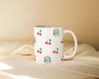White mug with cherry pattern and dog illustration on a beige surface