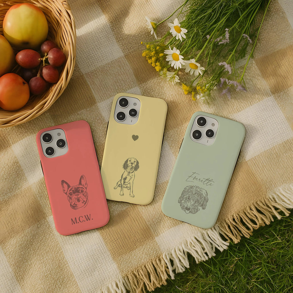Three phone cases with dogs on a checkered blanket with fruits and flowers.