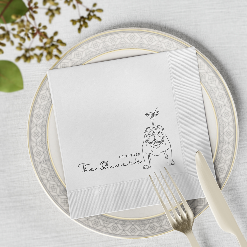 Cocktail napkin with bulldog illustration and 'The Oliver's' text on a place setting with plates and cutlery.