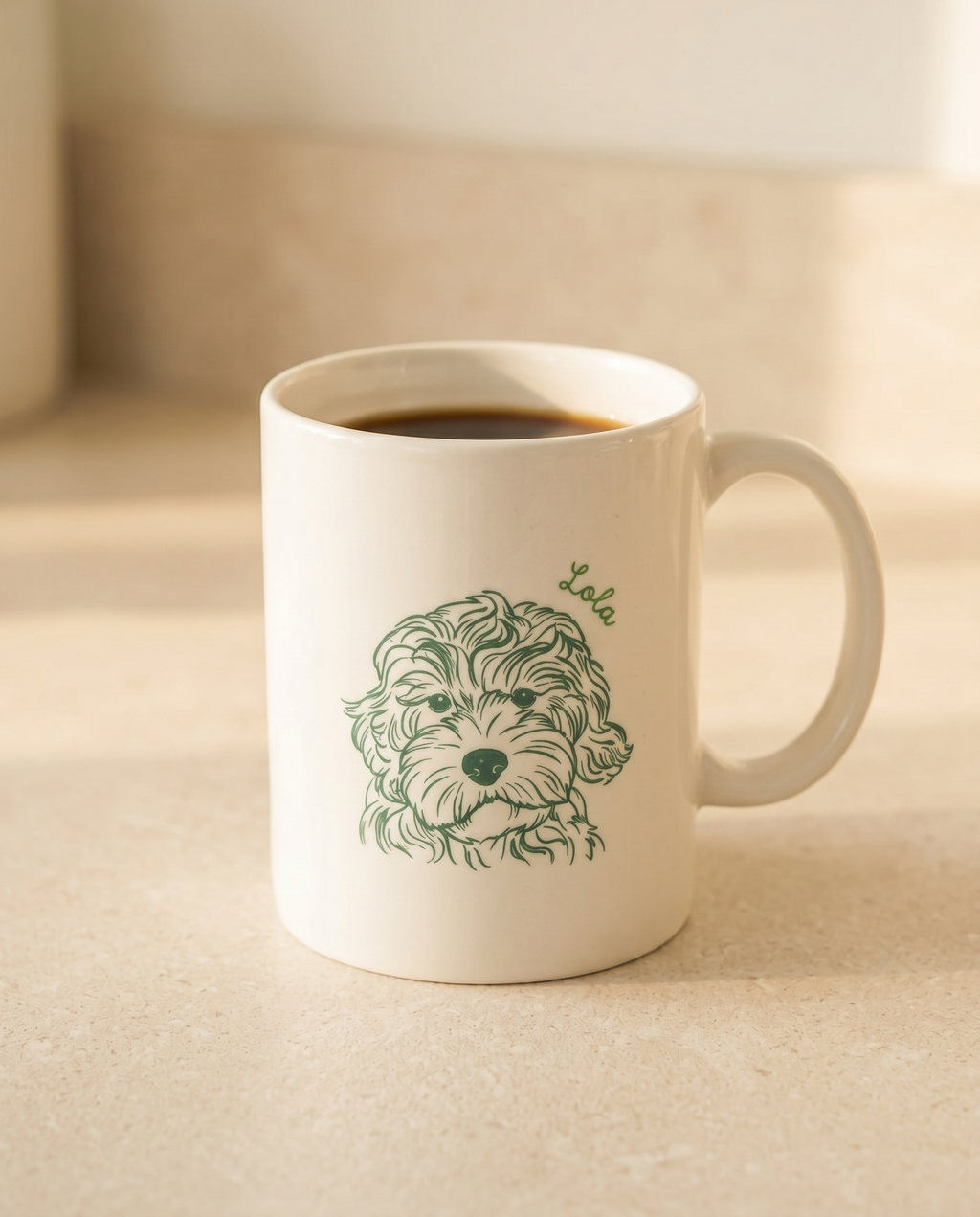 A white ceramic coffee mug filled with black coffee, featuring a green line art illustration of a curly-haired dog's face with the name 'Lola' written above it, set on a beige countertop.