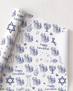 custom dog cat White wrapping paper with a blue Hanukkah-themed print featuring golden retriever dogs, menorahs, dreidels, stars, and the text 'happy hanukkah', shown partially unrolled on a white textured surface.