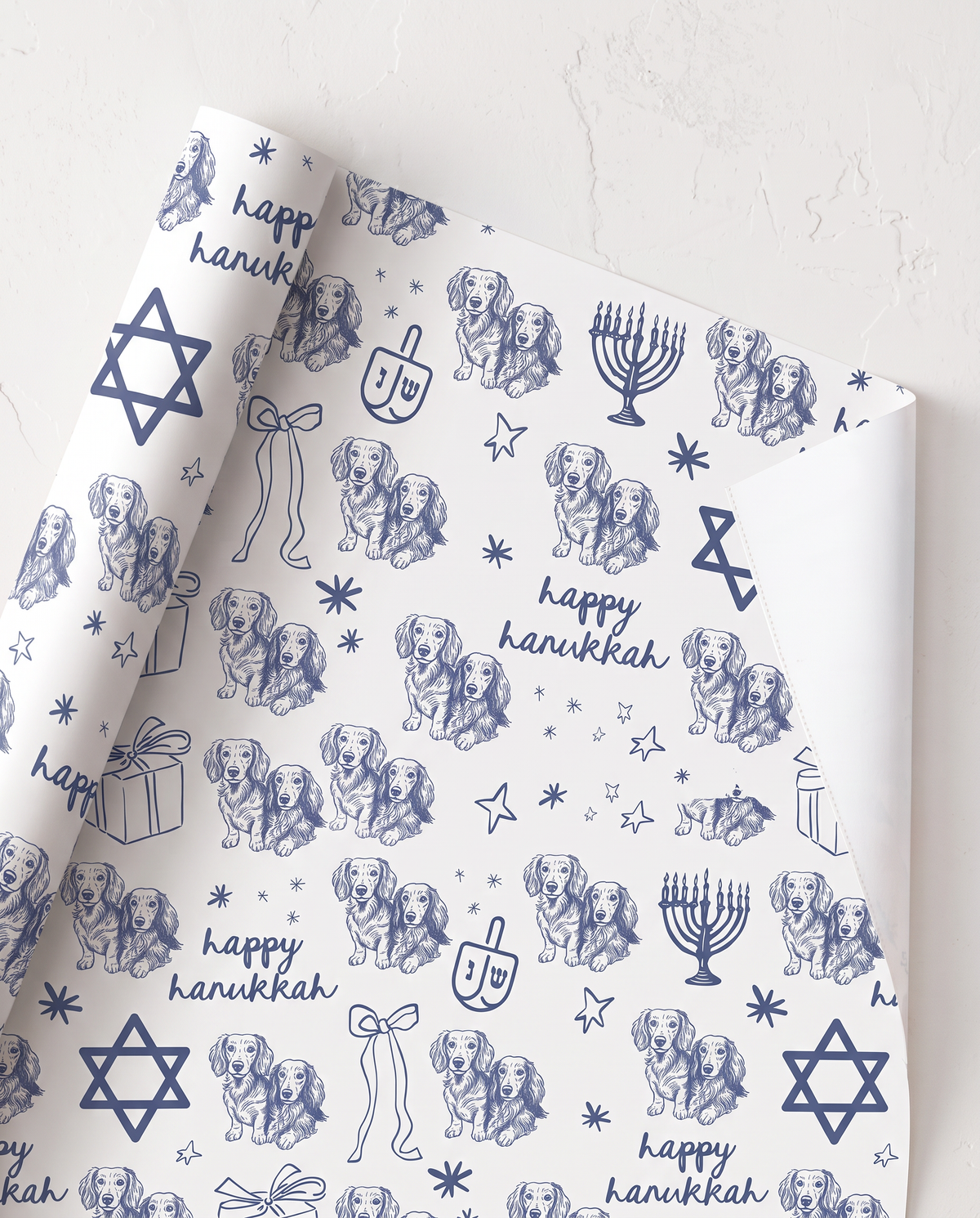 custom dog cat White wrapping paper with a blue Hanukkah-themed print featuring golden retriever dogs, menorahs, dreidels, stars, and the text 'happy hanukkah', shown partially unrolled on a white textured surface.
