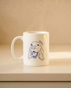 A white ceramic coffee mug with a blue line art illustration of a dog's face and the word 'Bodle' written above it, sitting on a beige surface against a matching beige background.