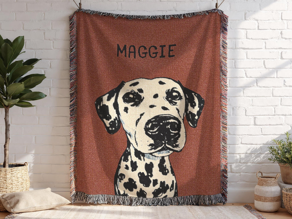 Blanket with a dalmatian dog illustration and 'Maggie' text, hanging on a white brick wall.