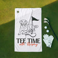 Golf towel with dog illustration and 'Tee Time with Ralphy' text on a green surface with golf accessories.