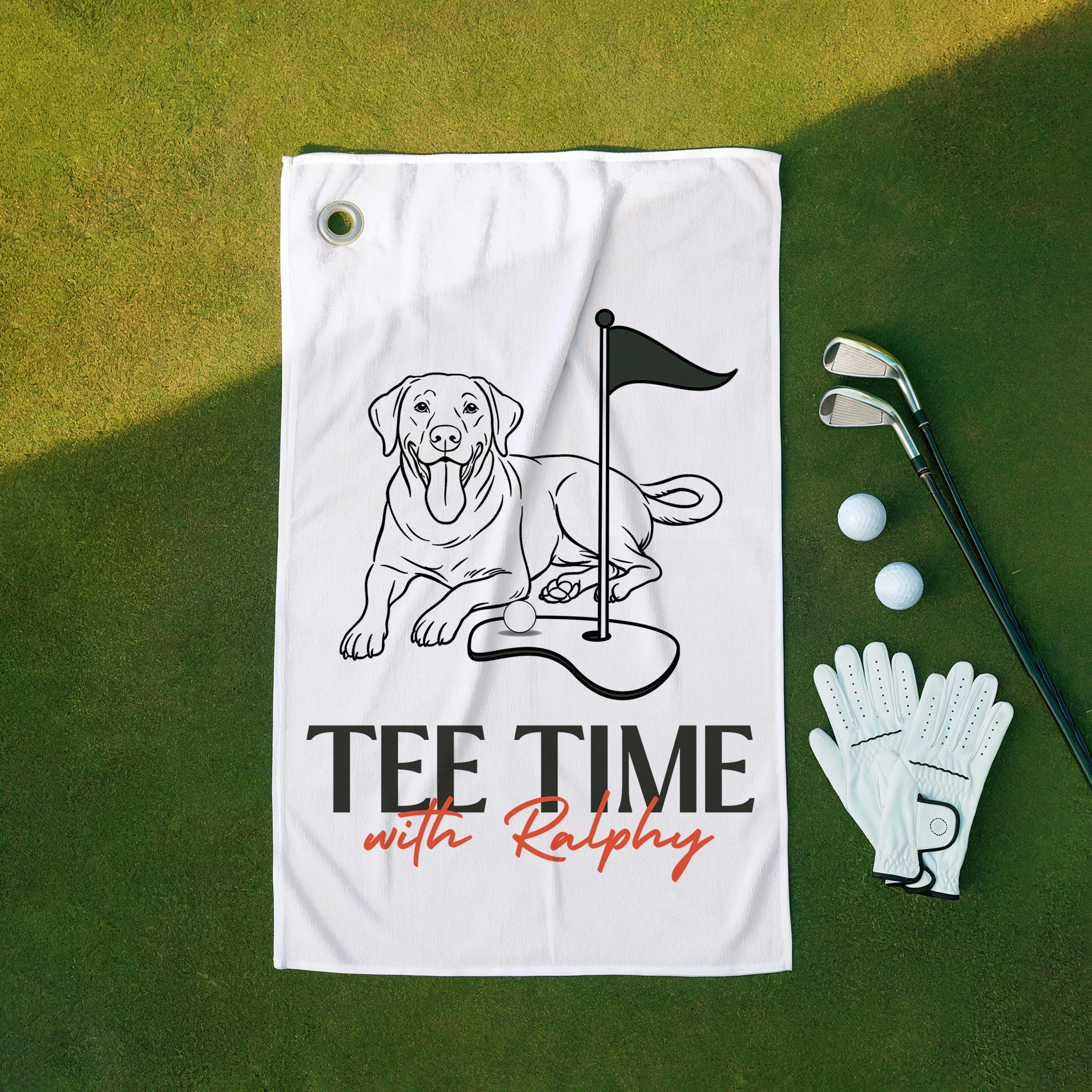 Golf towel with dog illustration and 'Tee Time with Ralphy' text on a green surface with golf accessories.