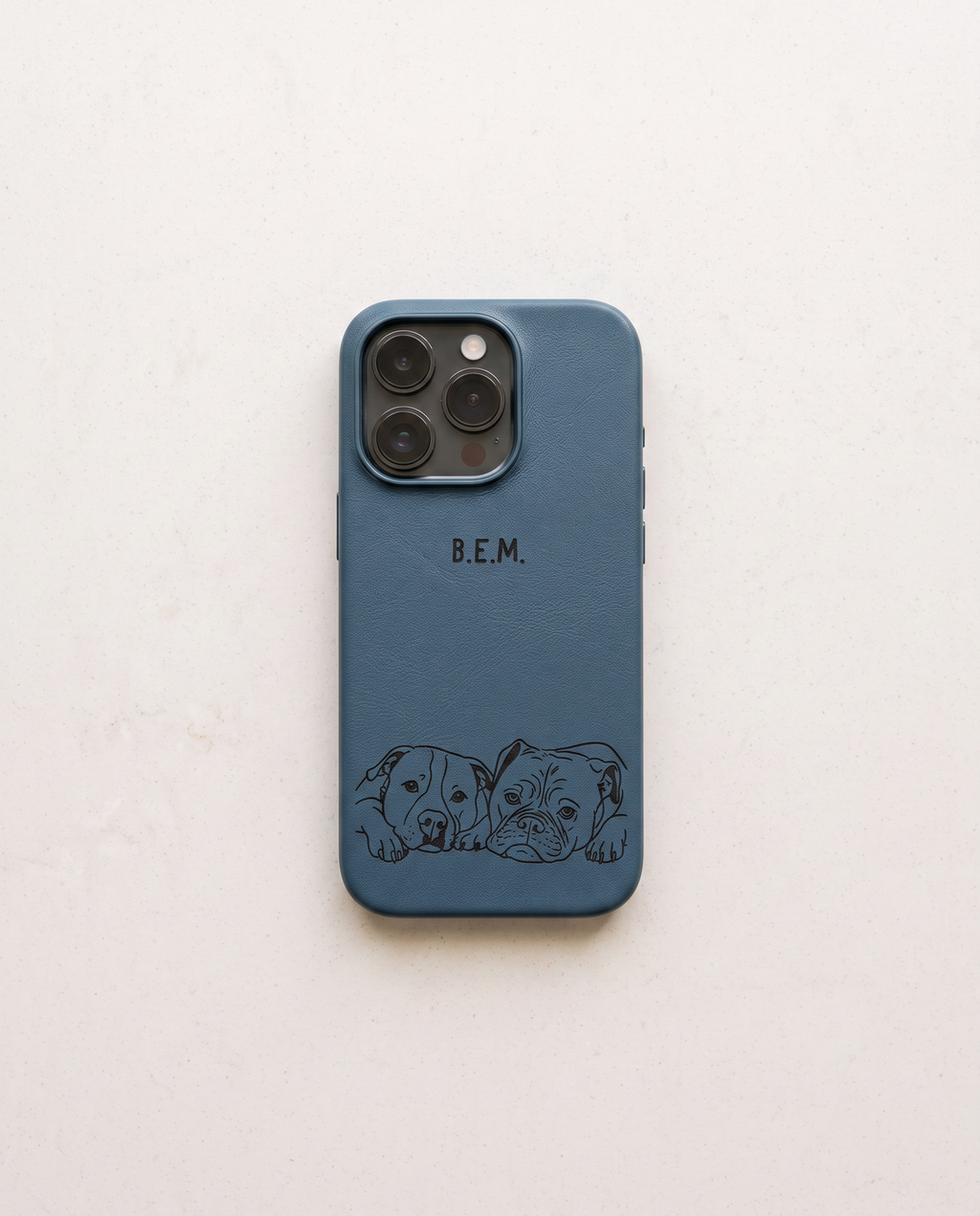 A slate blue phone case with a black engraved design of two puppies at the bottom and the initials 'B.E.