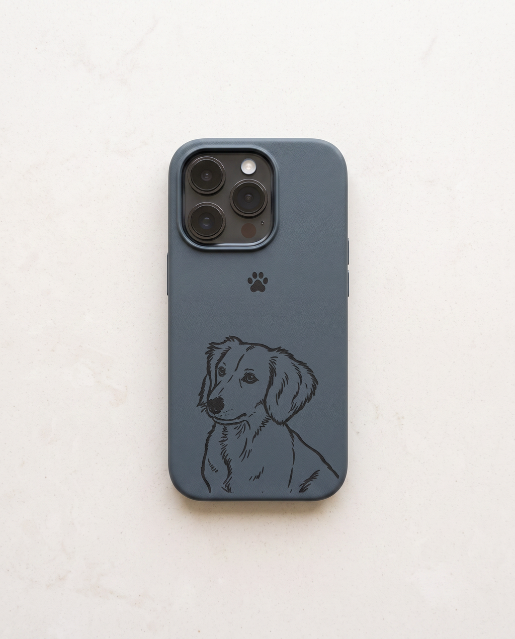 A blue leather phone case featuring a black line art illustration of a dachshund and a small black paw print, shown on a light beige textured background.