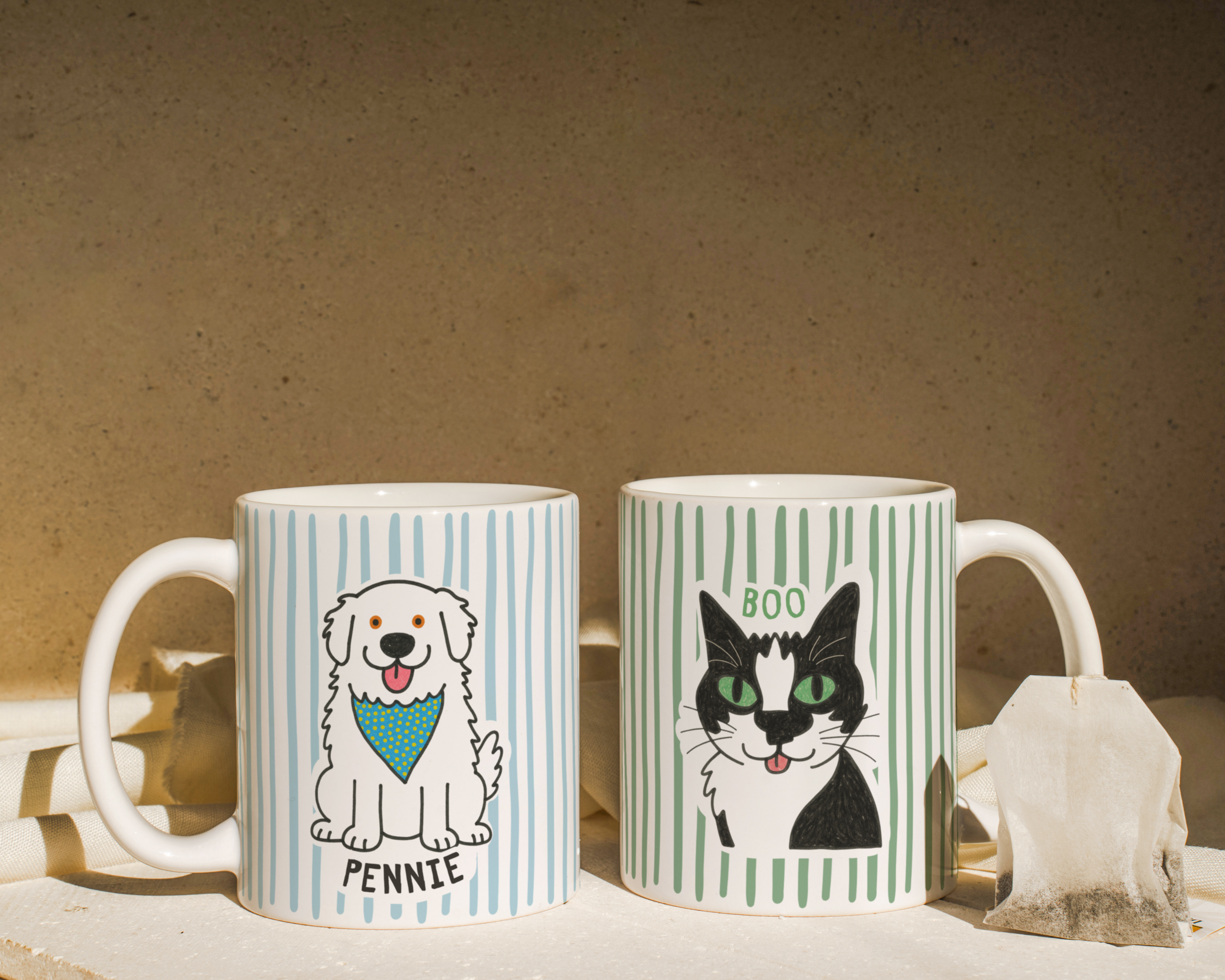 Two mugs with dog and cat illustrations on a textured surface