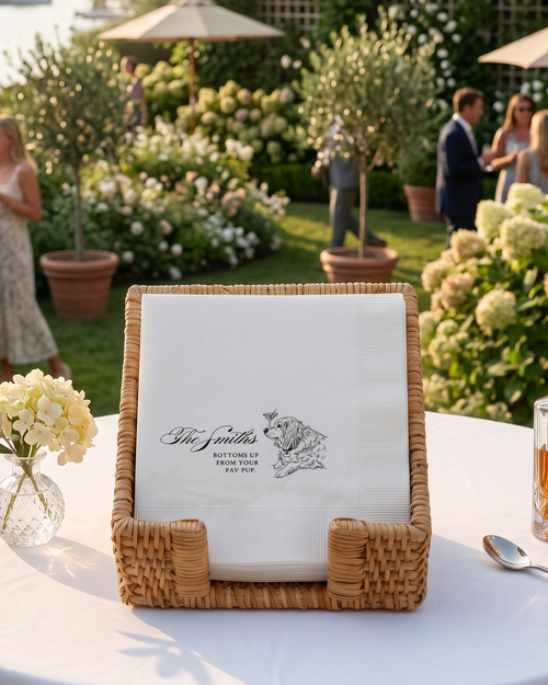 Outdoor garden wedding with a table and decorative items, including custom cockail napkins and a bottle.