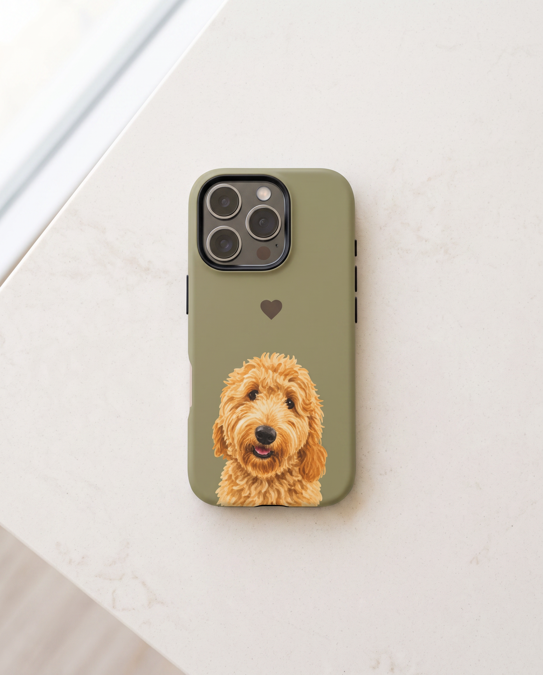 An olive green phone case featuring a printed portrait of a golden doodoodle dog and a small heart, shown on a light marble surface.