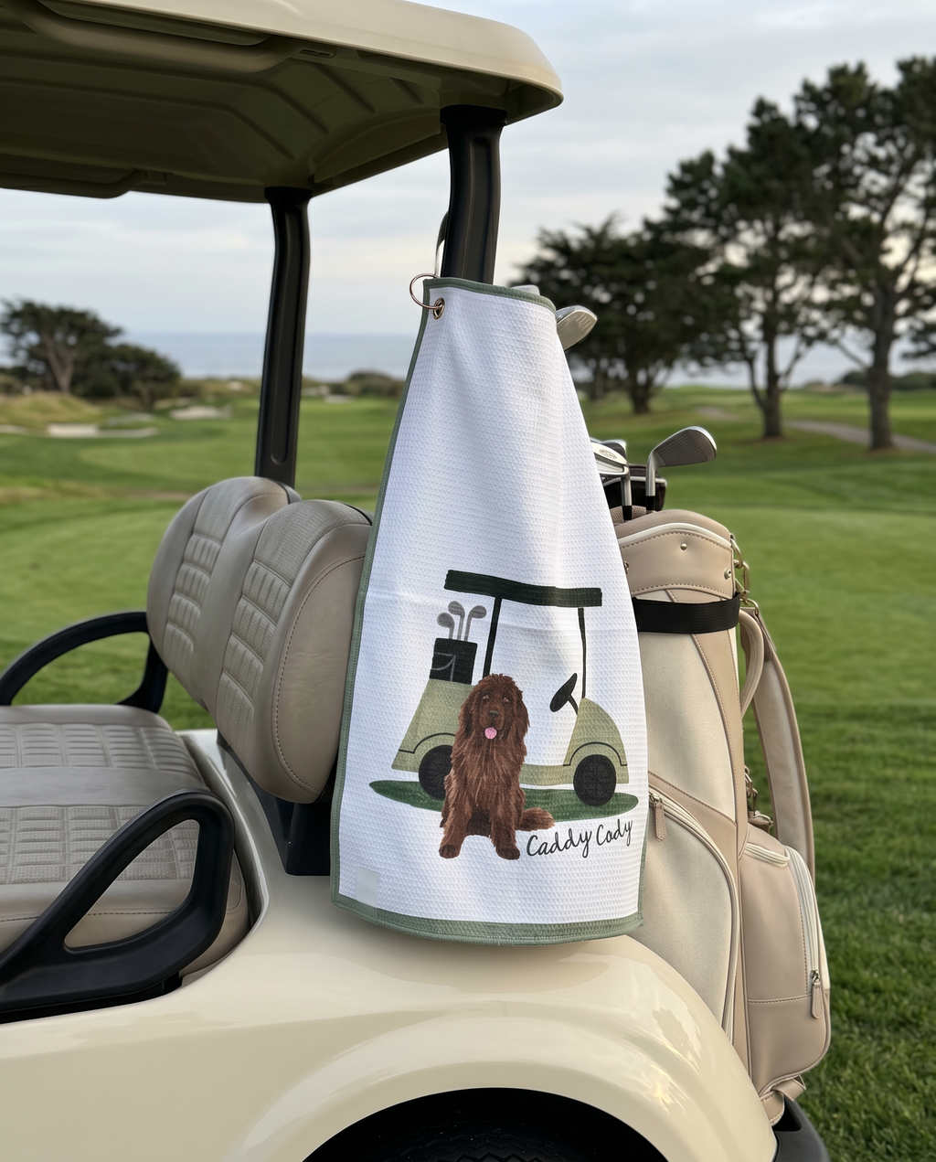 Golf towel with a dog design hanging from a golf cart on a golf course