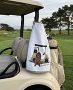 Golf towel with a dog design hanging from a golf cart on a golf course