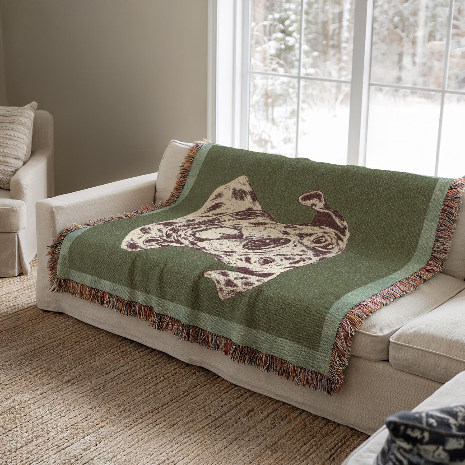Green blanket with a decorative pattern and dog draped over a white sofa in a living room.