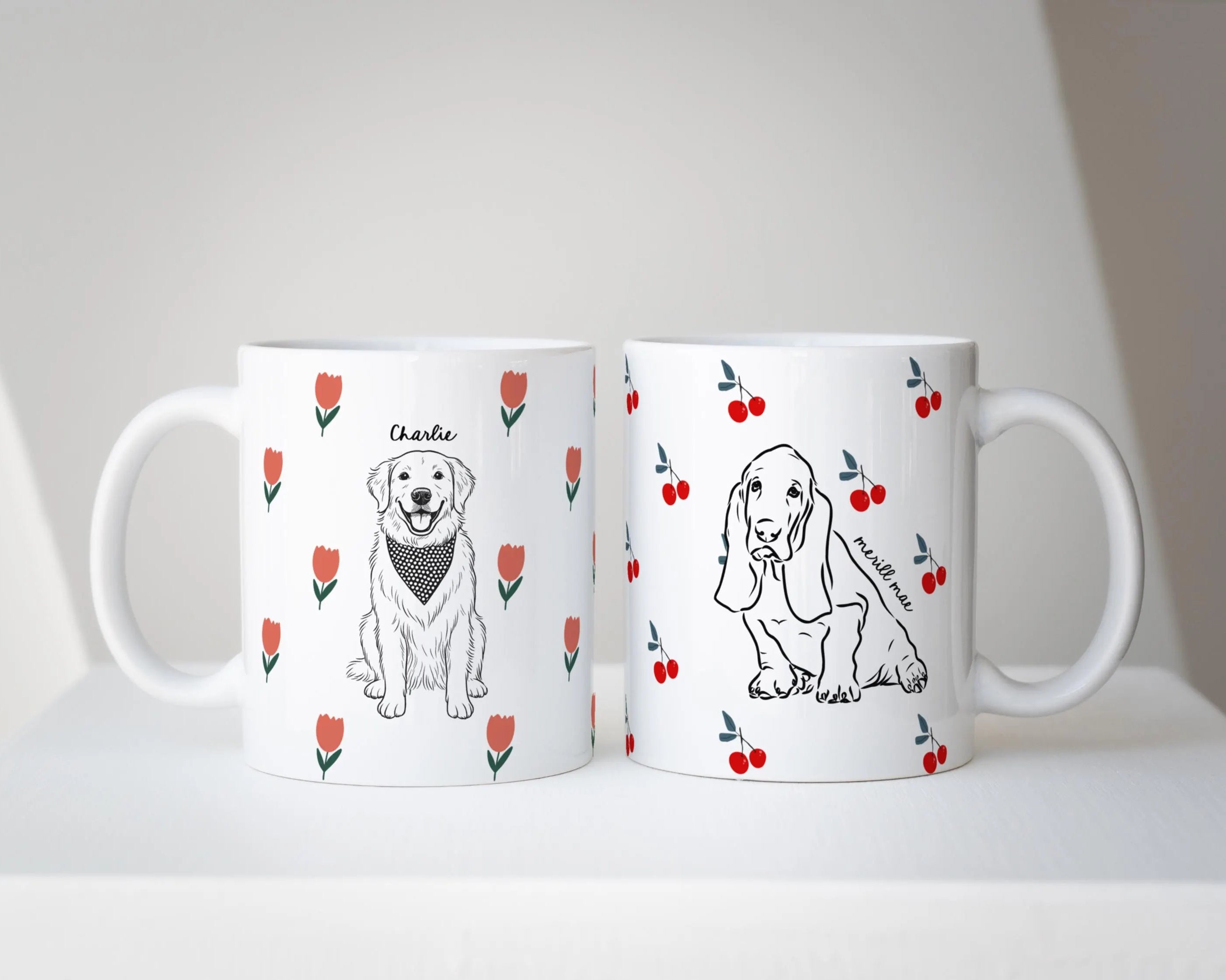 Two white mugs with dog illustrations and tulip flower pattern and cherry pattern on a white surface.