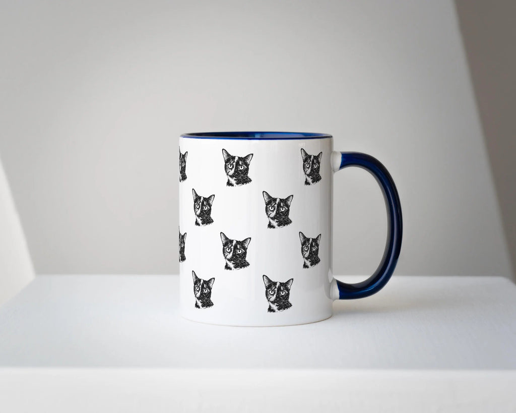 White mug with black cat pattern and blue handle on a white surface