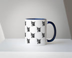 White mug with black cat pattern and blue handle on a white surface