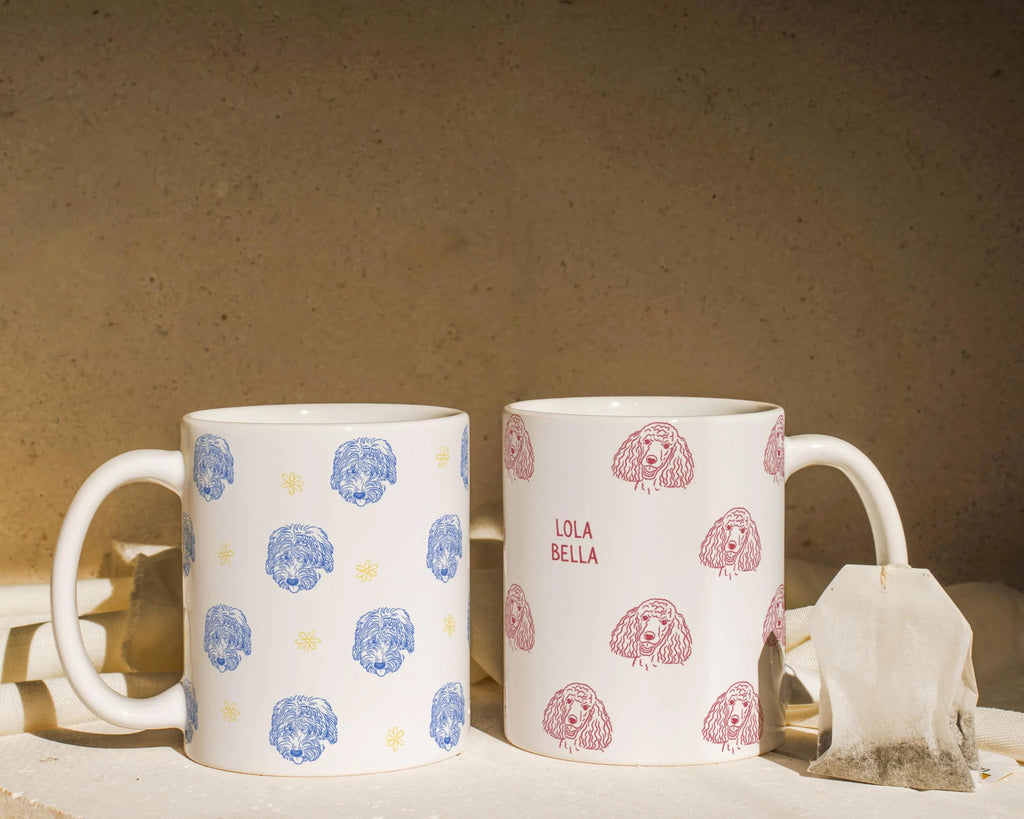 Two ceramic mugs with dog drawing patterns on a neutral background