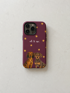 A phone case with a deep purple background, decorated with small gold stars, the text 'al. & opi', and two dachshund illustrations at the bottom, shown on a light textured surface.