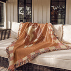 Orange and pink checkered throw blanket with cat illustration on a white outdoor sofa