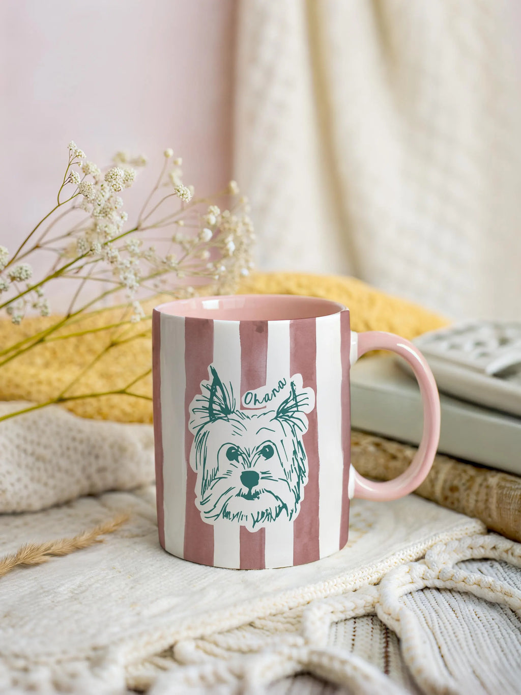 pink striped mug with a dog illustration on a cozy surface with flowers and a blanket.