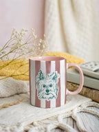 pink striped mug with a dog illustration on a cozy surface with flowers and a blanket.