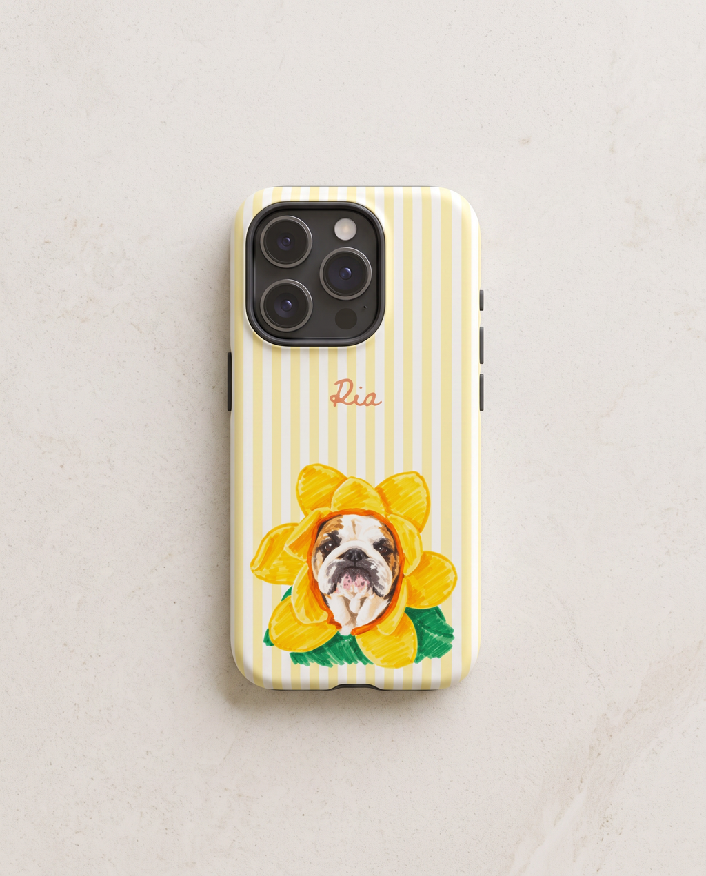 A phone case with pale yellow and white vertical stripes, featuring a yellow flower with a bulldog's face inside, green leaves, and the name 'Ria' in pink script near the top.