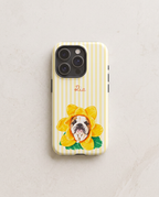 A phone case with pale yellow and white vertical stripes, featuring a yellow flower with a bulldog's face inside, green leaves, and the name 'Ria' in pink script near the top.
