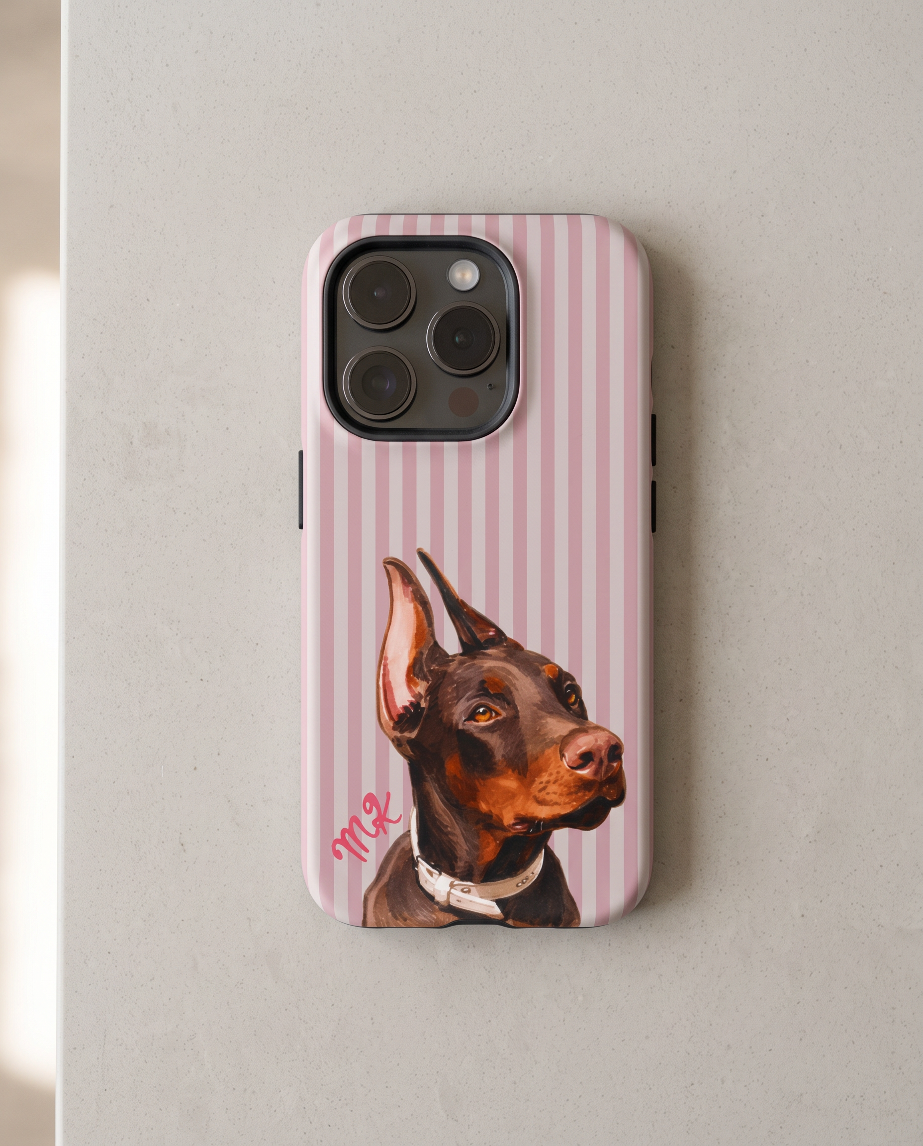 A pink and white vertically striped phone case featuring a painted portrait of a Doberman dog, shown on a light gray textured surface.