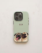 A sage green phone case featuring a printed illustration of two pug dogs at the bottom and the initials 'E.C.