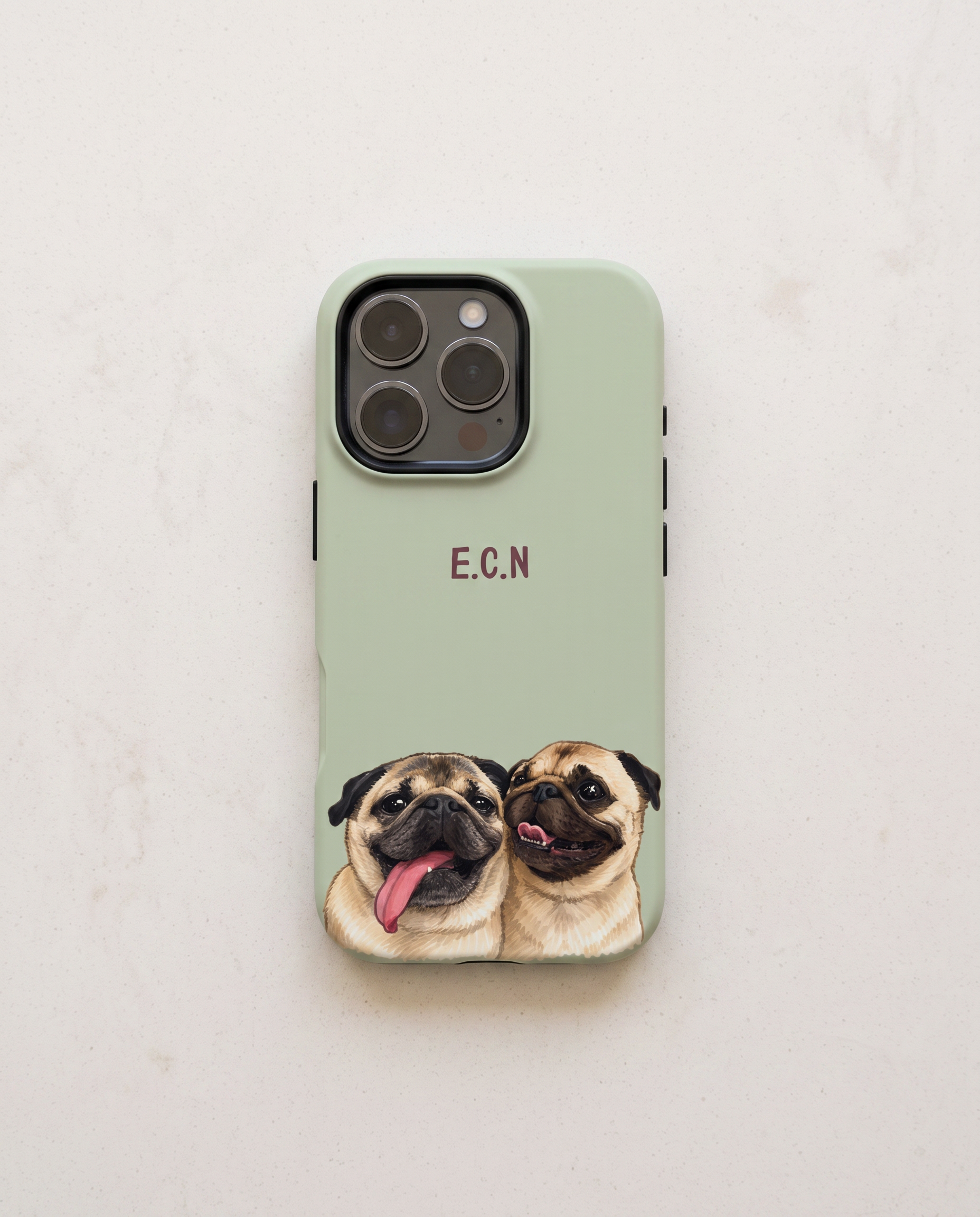 A sage green phone case featuring a printed illustration of two pug dogs at the bottom and the initials 'E.C.