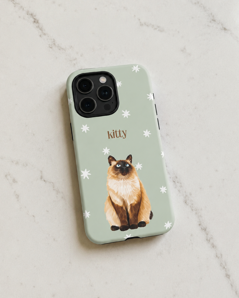 A sage green phone case featuring a watercolor illustration of a Siamese cat and the name 'kitty' in brown, shown on a light marble background.