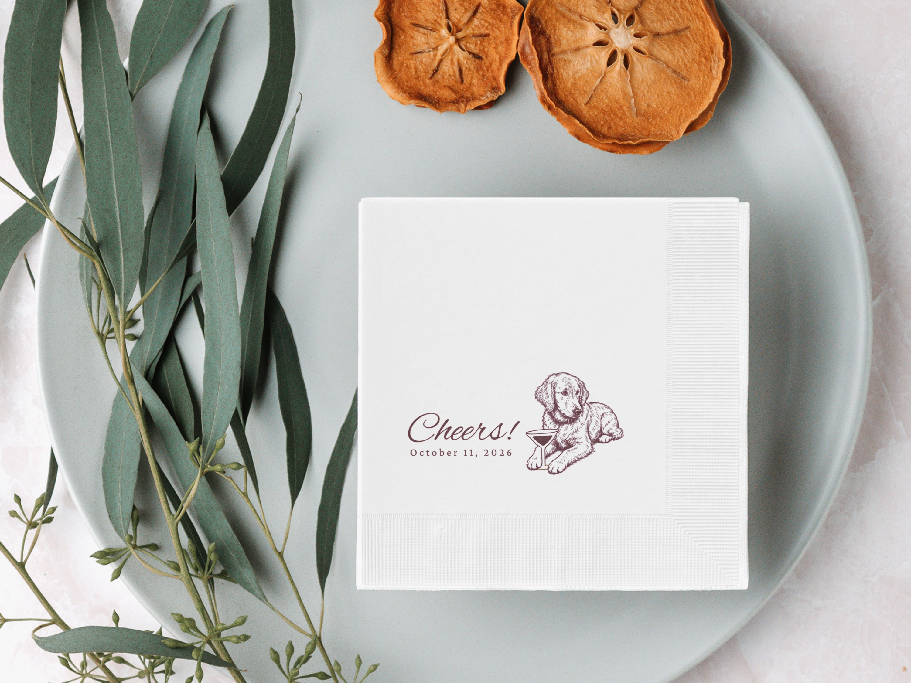 White napkin with a printed design on a gray plate with dried oranges and eucalyptus leaves.