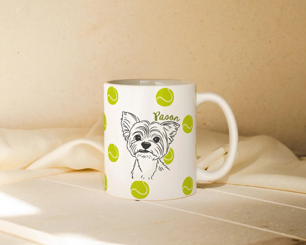 White mug with custom dog illustration and tennis ball icons on a beige surface