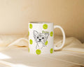 White mug with custom dog illustration and tennis ball icons on a beige surface