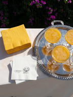 Silver tray with orange juice glasses, yellow napkins, and a napkin with a dog illustration on a white surface.